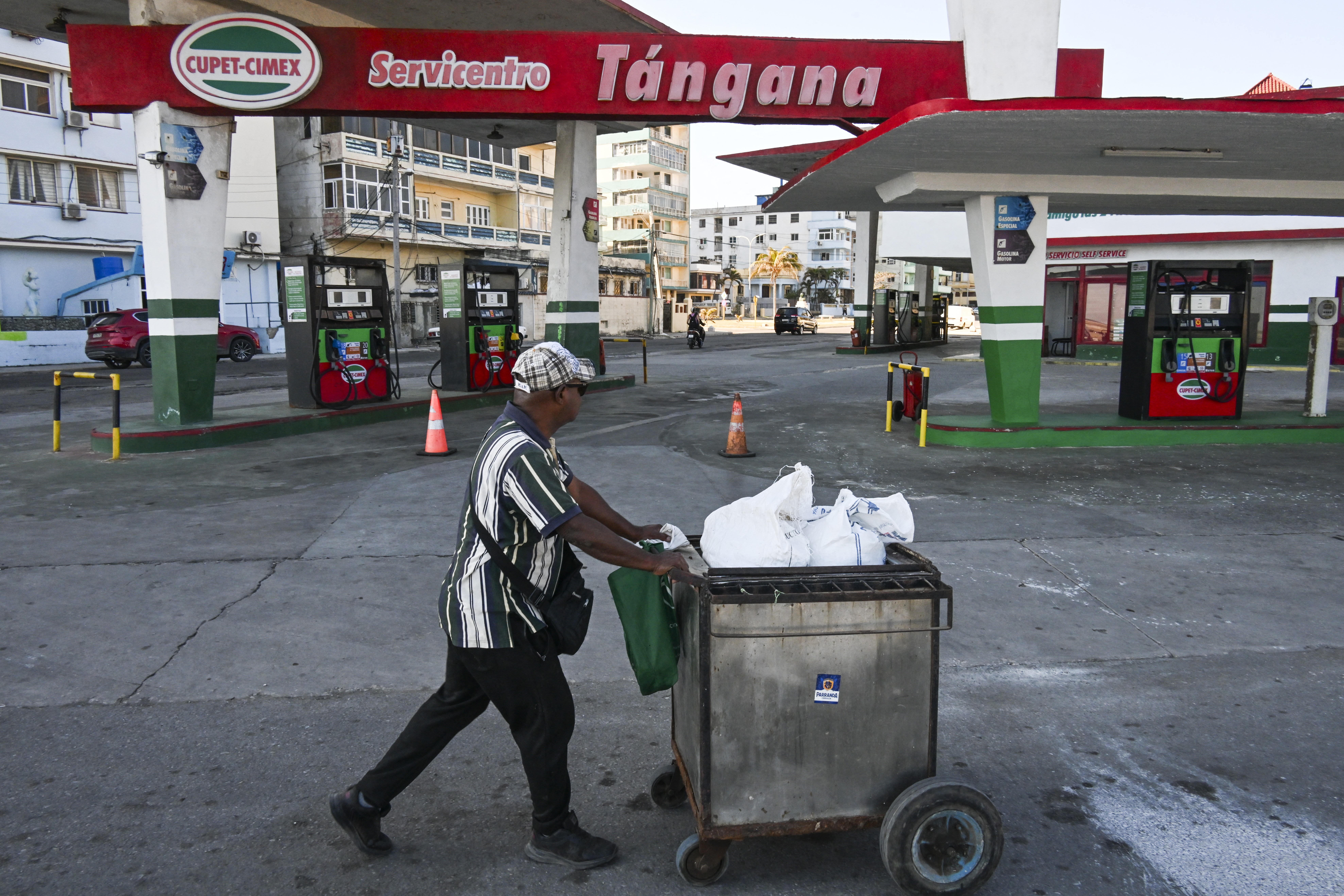 A man pushes his cart past an empty gas station.