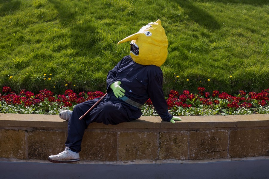 A person wearing a costume with a lemon-shaped head sits on a low bench.