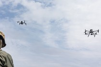 A soldier and two flying military drones.