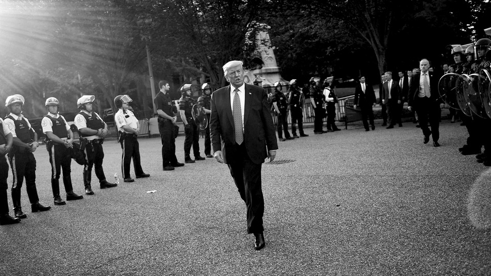 Donald Trump, with police officers behind him, walks outside the White House. The photo is black and white.