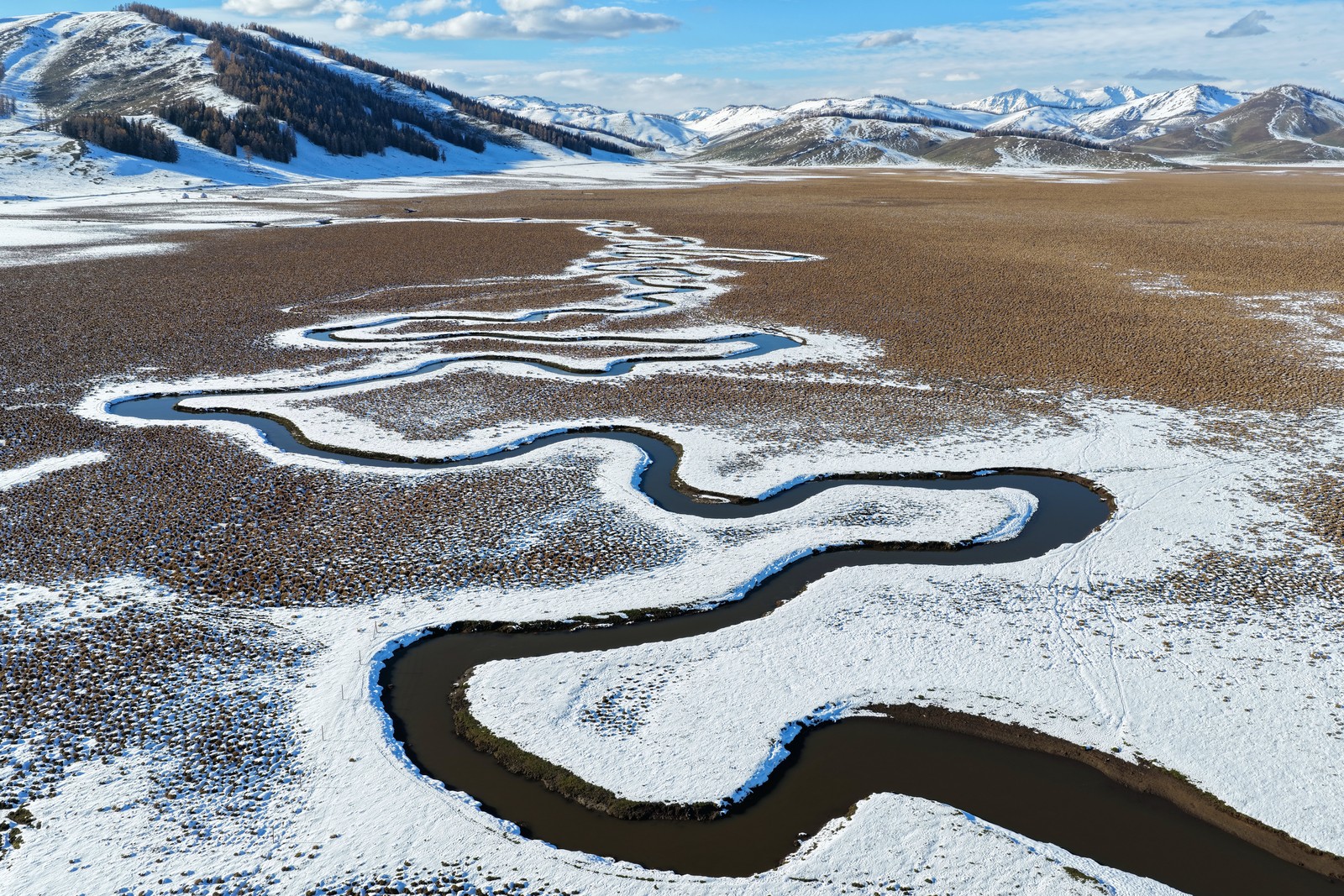 A meandering river runs through a grassy, snow-covered valley.