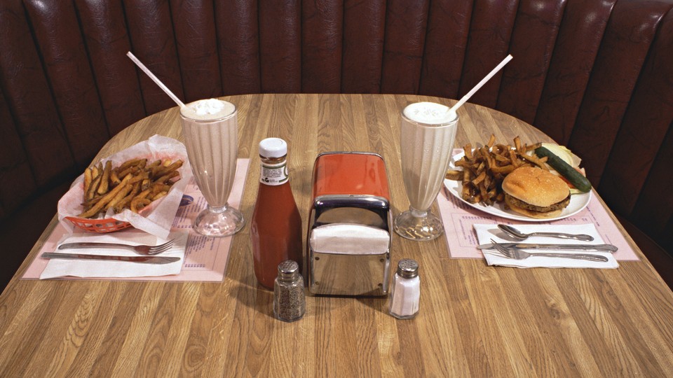 A table at a diner with a hamburger, french fries, milkshakes, and ketchup