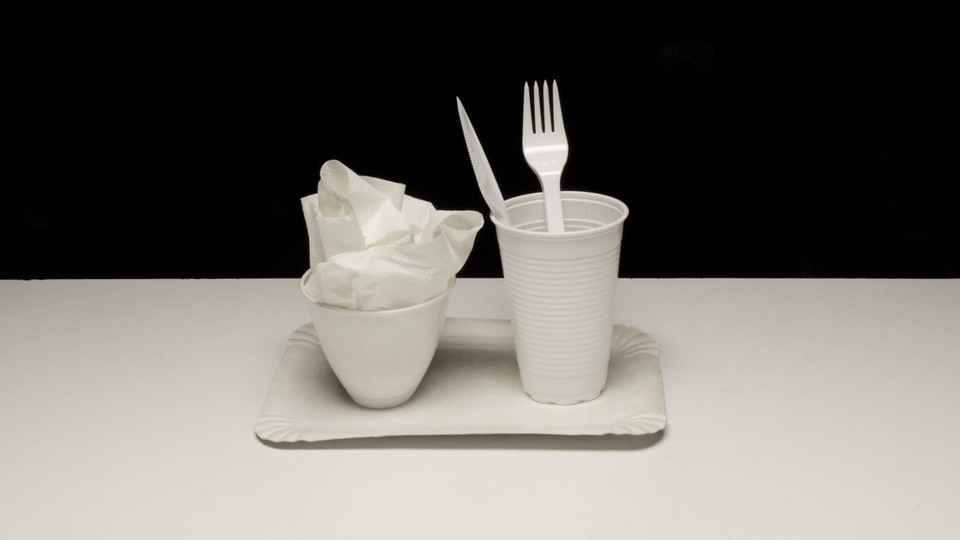 two plastic cups, a plastic tray, a plastic fork and knife, and crumpled plastic wrap