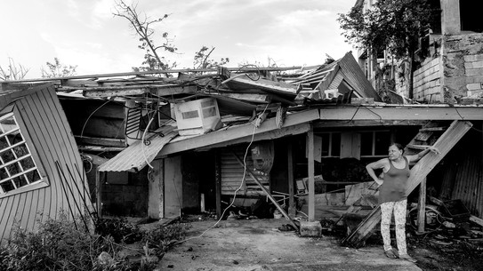 A woman in Puerto Rico stands beside a devastated home.