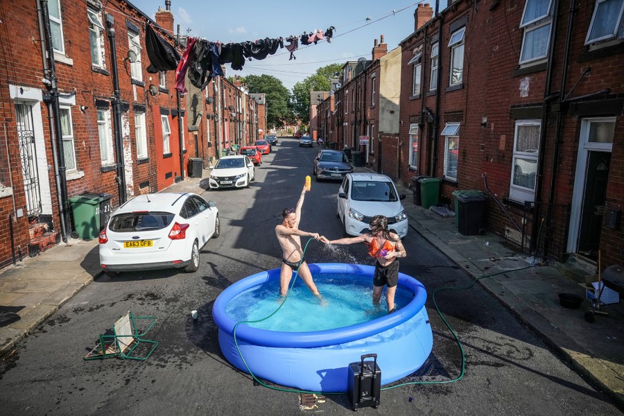 Two people play in a small paddling pool set up in a residential street.