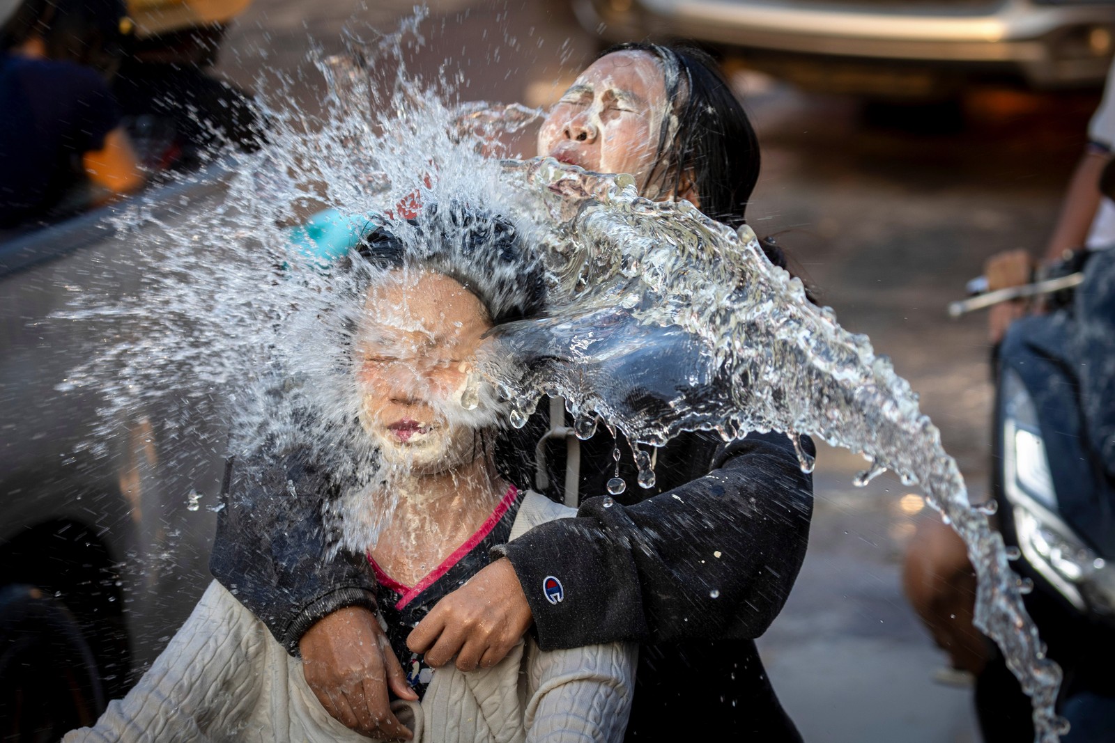Two people react as they are hit in the face by water thrown at them during a water festival.