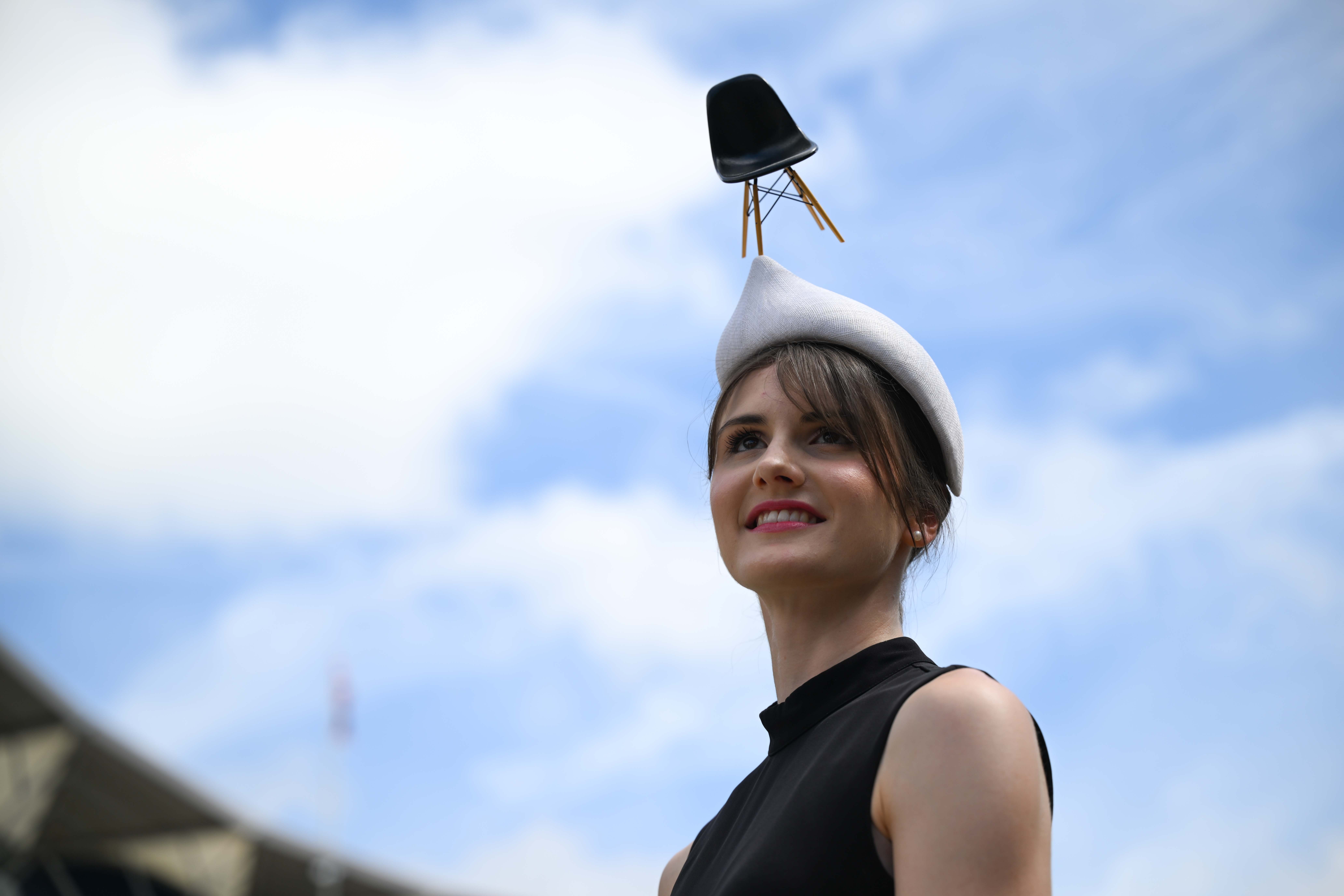 A person poses for a photo, wearing a fashionable cap with a tiny chair attached to the top of it.