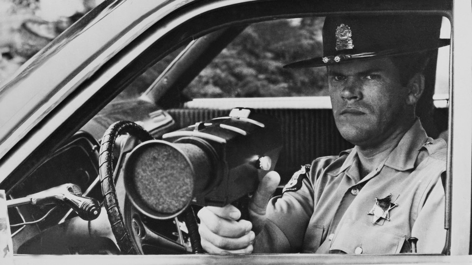 A police  officer uses a radar gun through a window of a car