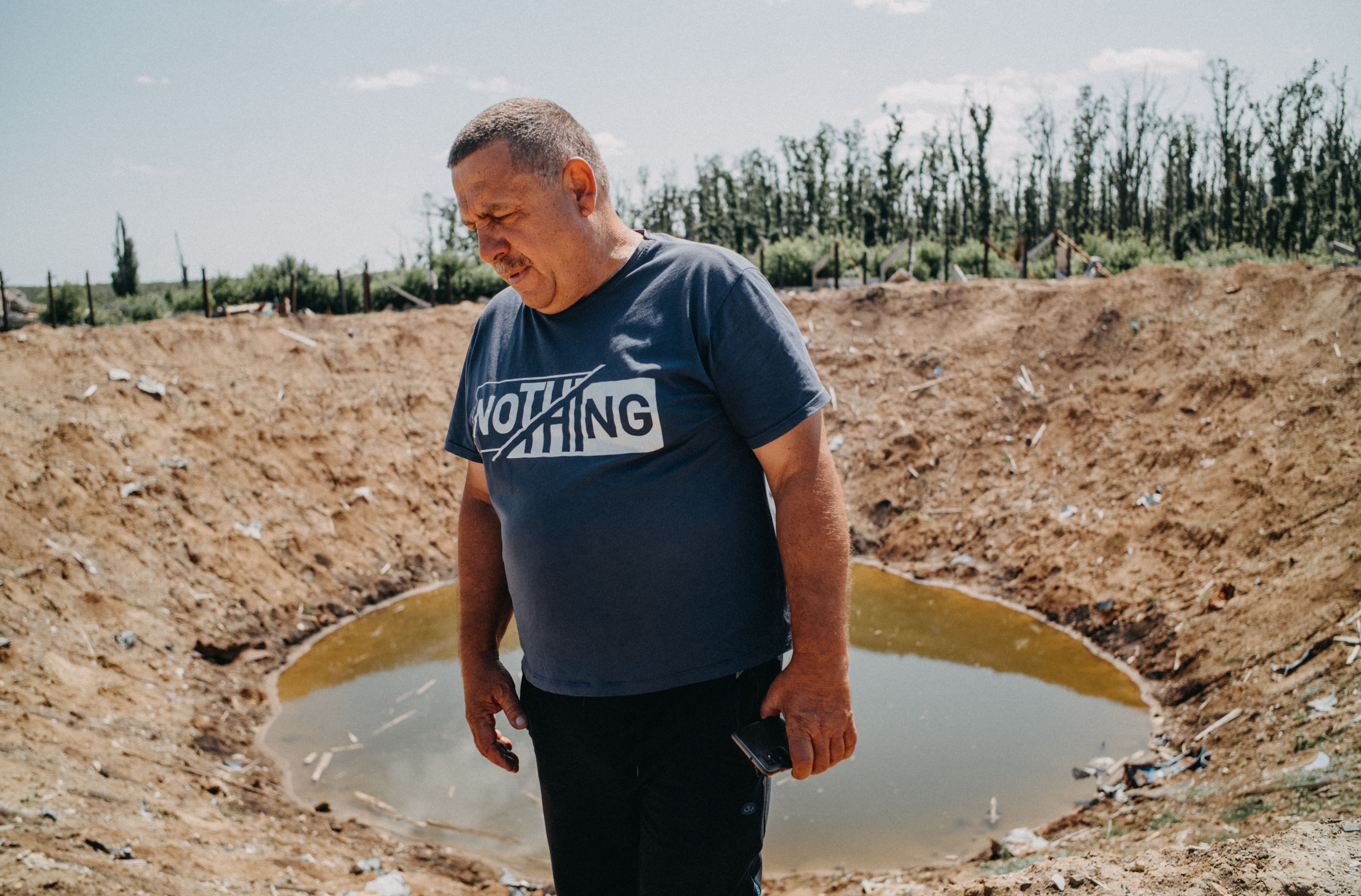 A farmer walks beside a crater as he surveys his destroyed farm.