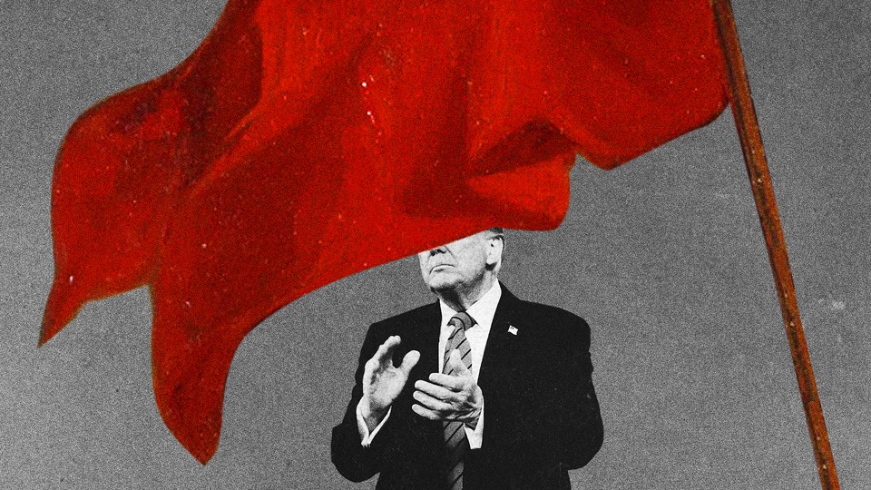 Photo of a man in a suit clapping with a huge red flag in the foreground, covering half his face.