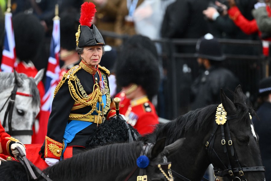 Princess Anne, in dress uniform, rides a horse along a parade route.
