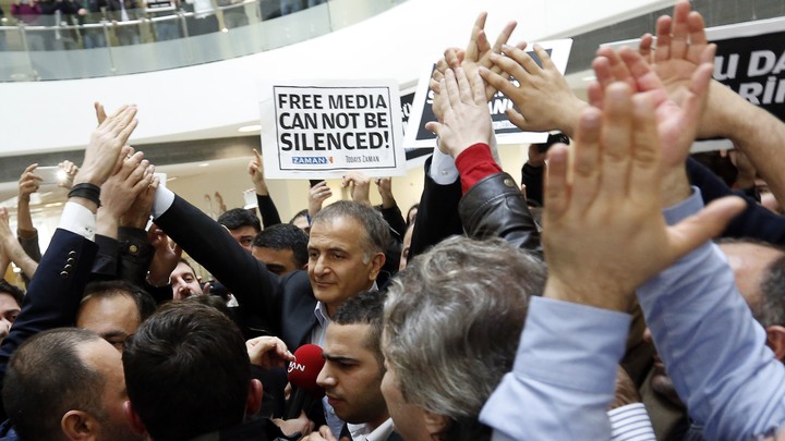 The Zaman editor in chief, Ekrem Dumanli, stands in a crowd of supporters and newspaper employees holding signs that say, in English and Turkish, "Free media cannot be silenced."