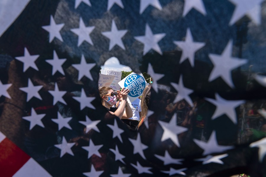 A hole in an American flag frames a protester holding a sign that reads "Keep abortion legal."