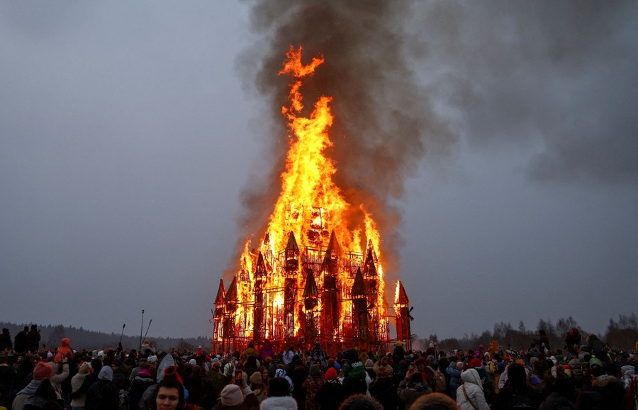 A crowd gathers around a burning temporary wooden structure during a festival.