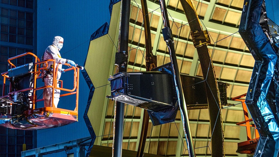 A picture of a technician examining the James Webb Space Telescope and its gold-covered mirrors