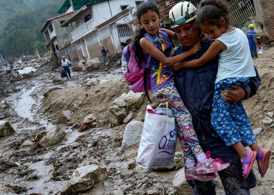 A firefighter carries two girls in a flood-damaged town.