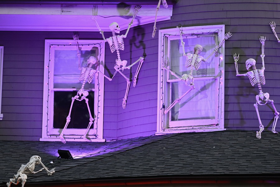 Half a dozen plastic skeleton decorations appear to climb up the outside of a house.