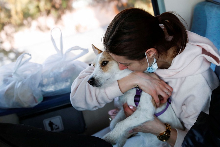 A woman embraces a small dog while while sitting inside a train.