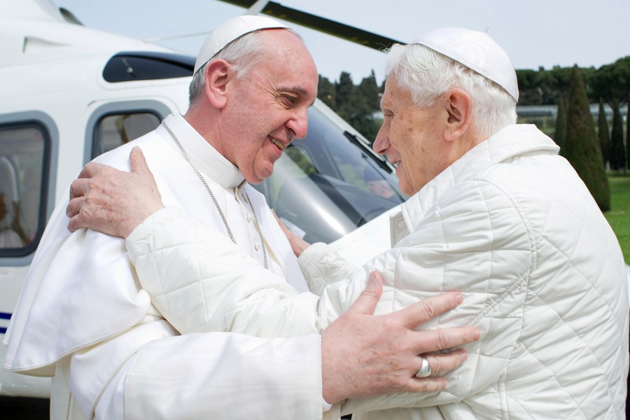 Pope Francis embraces Pope Emeritus Benedict XVI beside a helicopter.
