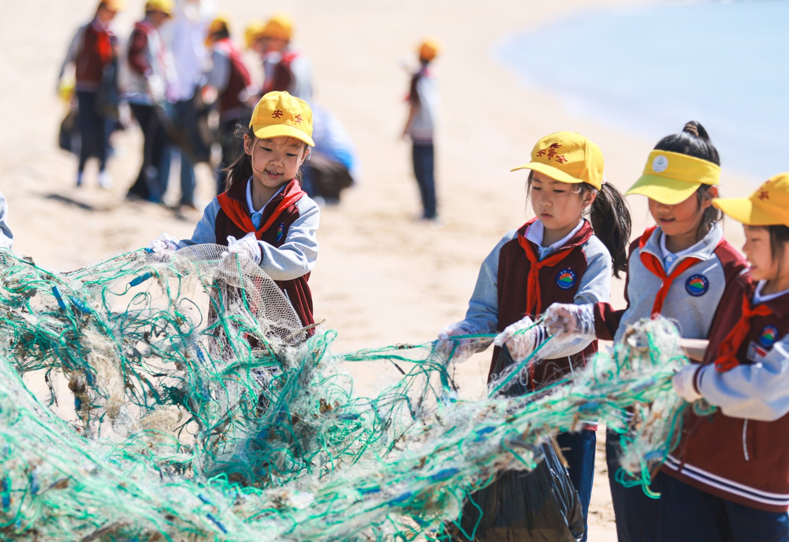 Several school children work together to remove abandoned netting from a beach.