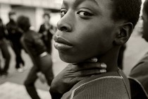 A boy looks directly at the camera, covering his neck with his hand