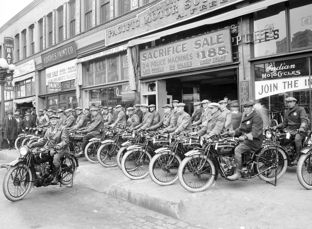 A black-and-white photo from 1922 shows a row of men seated on motorcycles parked on a sidewalk.