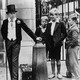 A black-and-white photo depicting local boys staring at Harrow schoolboys in coats and top hats.
