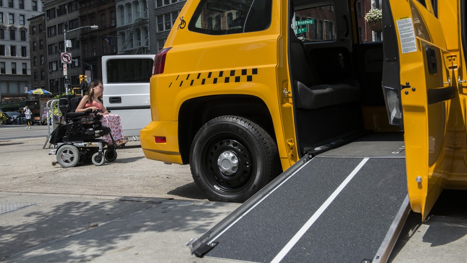 A woman in a wheelchair rolls past a taxi with an open ramp.