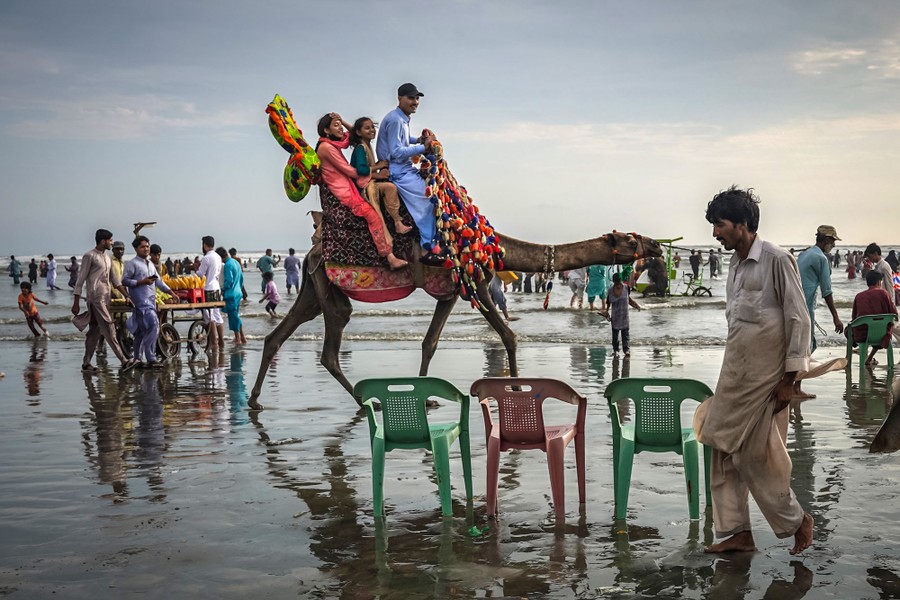 People ride a camel along a beach, among many other beachgoers.