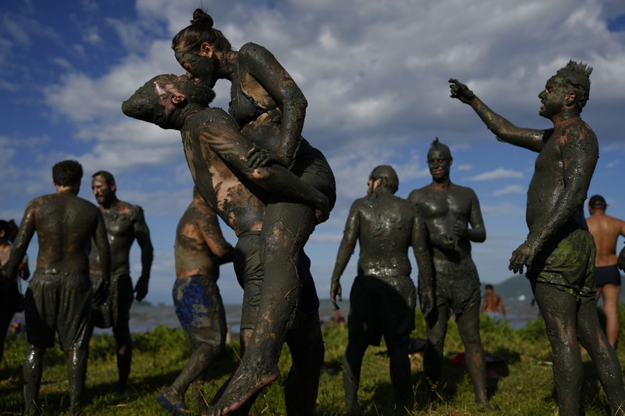 A couple embraces and shares a kiss, among several others—all completely covered with dark mud.