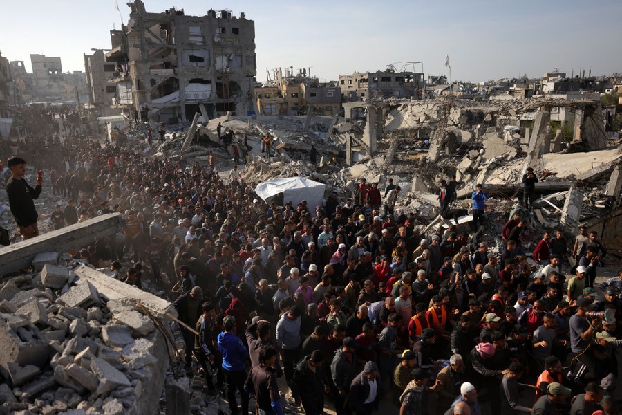 Palestinians take part in an anti-Hamas protest, marching in a street surrounded by shattered buildings.