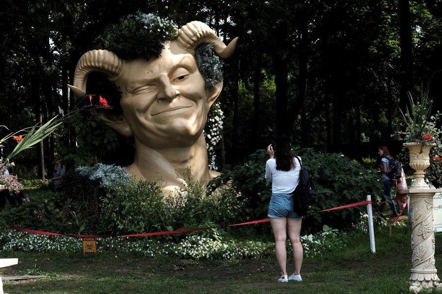 A woman takes a picture of a sculpture depicting Puck.
