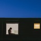 Picture of a building window showing a lonely woman using laptop