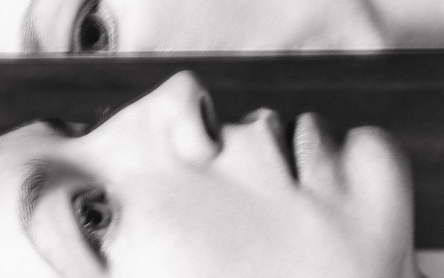 A woman's upturned face half-reflected in a mirror