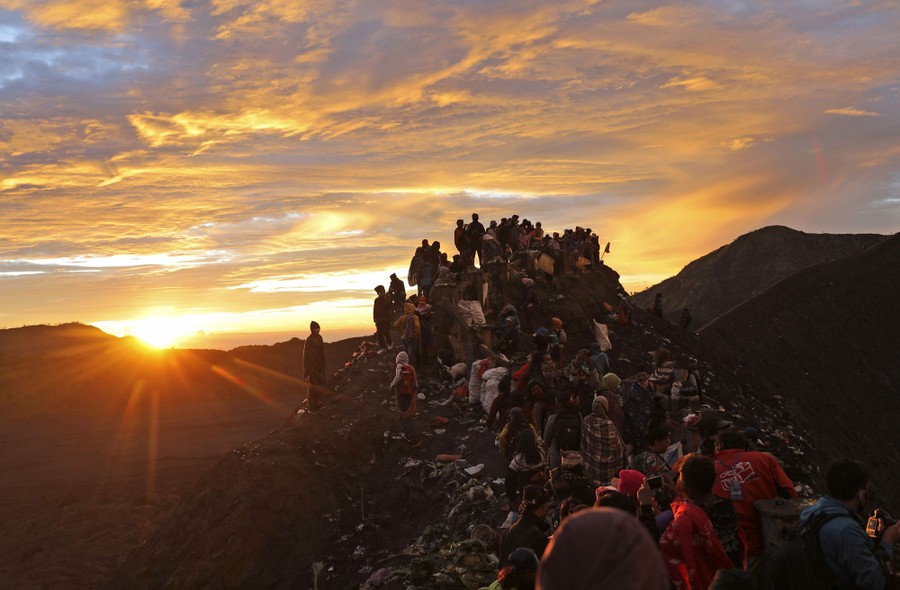 A crowd of worshippers gathers on the lip of a volcanic crater at dawn.