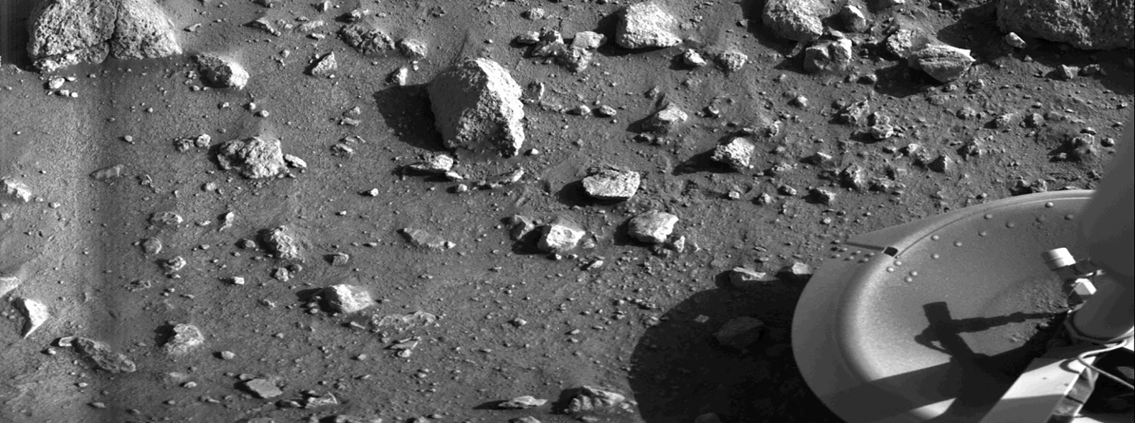 Rocky, sandy ground, seen on Mars, beside the footpad of a lander