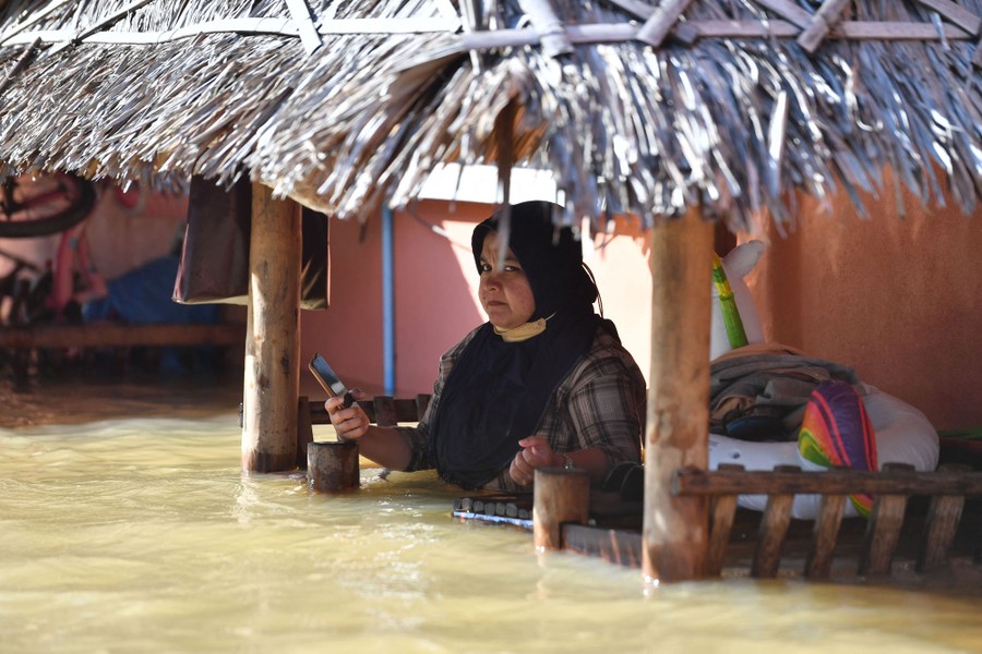 A woman is seen in deep floodwater, under a porch, holding a phone.