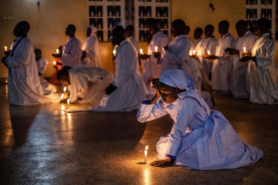 Worshippers kneel with candles inside a church.