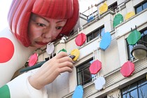 A large inflatable ballon figure shaped like a person hangs over the side of a building, appearing to paint polka dots on the facade.