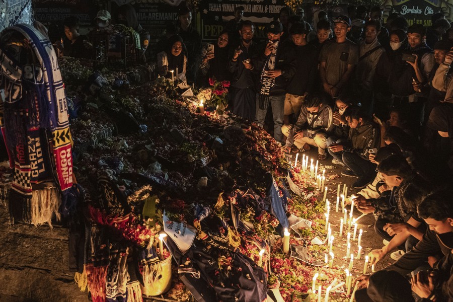 A crowd gathers before a makeshift memorial, lighting candles.