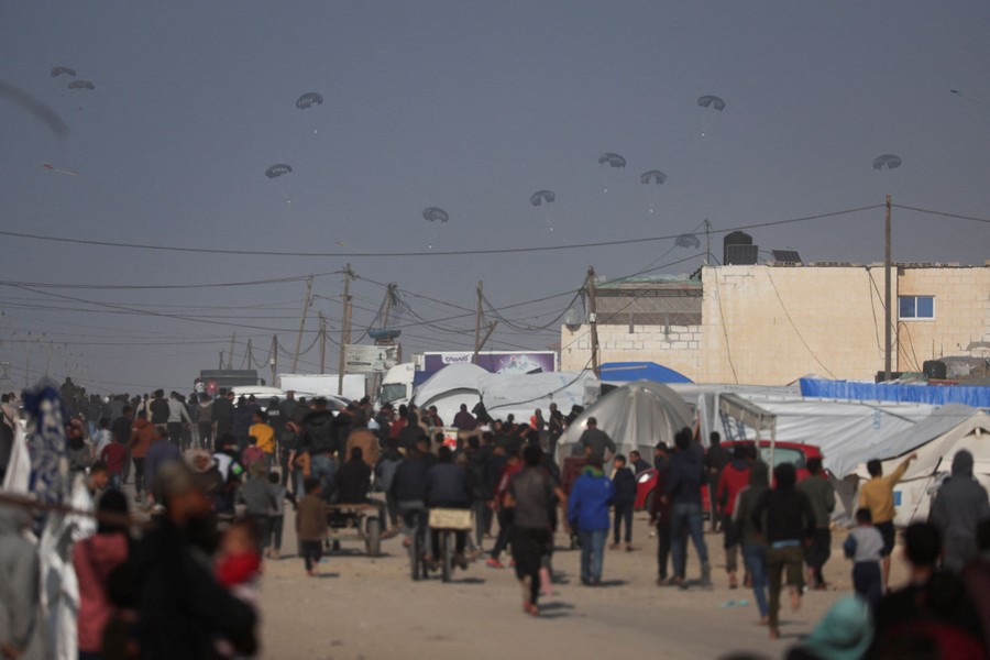 Palestinians walk and run toward about a dozen distant parachutes that carry crates of aid.