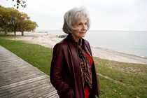 Alice Munro walks in front of a river and looks off to the right