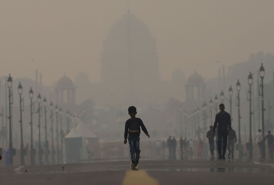 A boy walks on a road in front of a palace on a smoggy day.