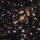 A field of galaxies on the black background of space. In the middle is a collection of dozens of yellowish galaxies that form a foreground galaxy cluster.