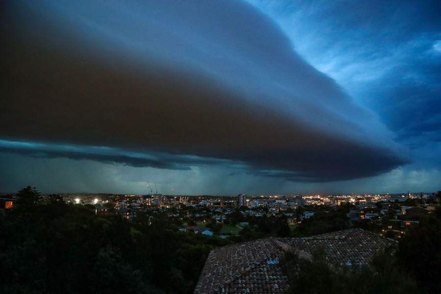 A dark, well-defined cloud looms above a cityscape.