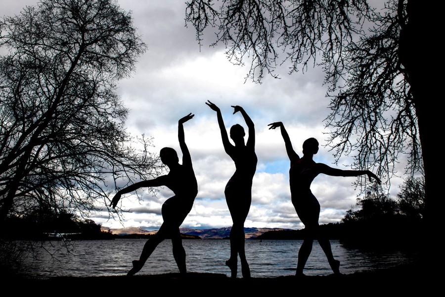 Three ballet dancers pose in front of a lake.