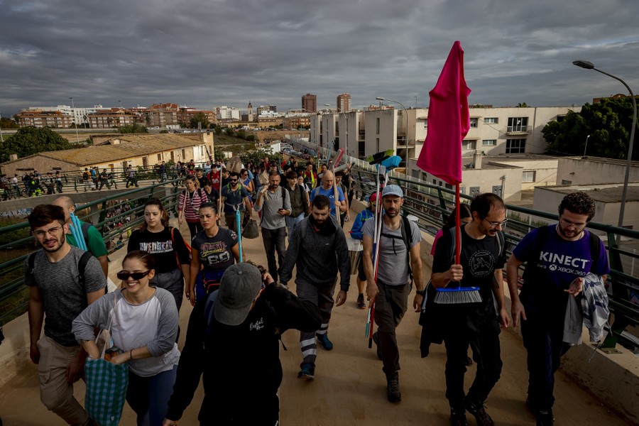 Dozens of people carrying brooms and shovels walk on an elevated walkway.