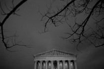 A photo of the Supreme Court building set against a dark and cloudy sky with bare tree branches framing it in the foreground