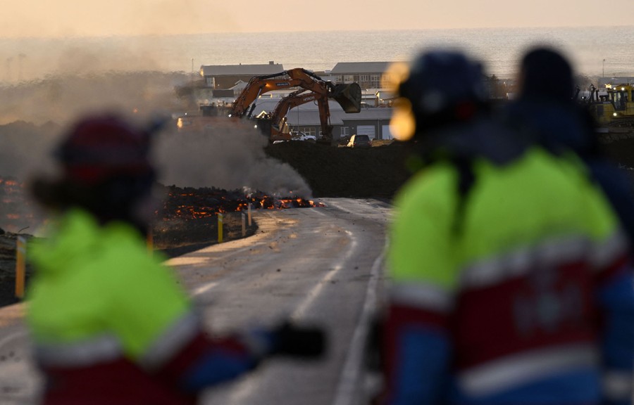 Several people watch as others use excavators to finish a dirt berm.