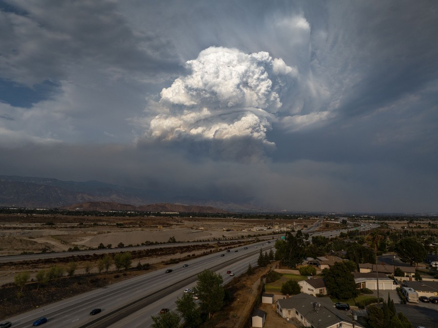 A huge white cloud rises above a wildfire burning on distant hills.